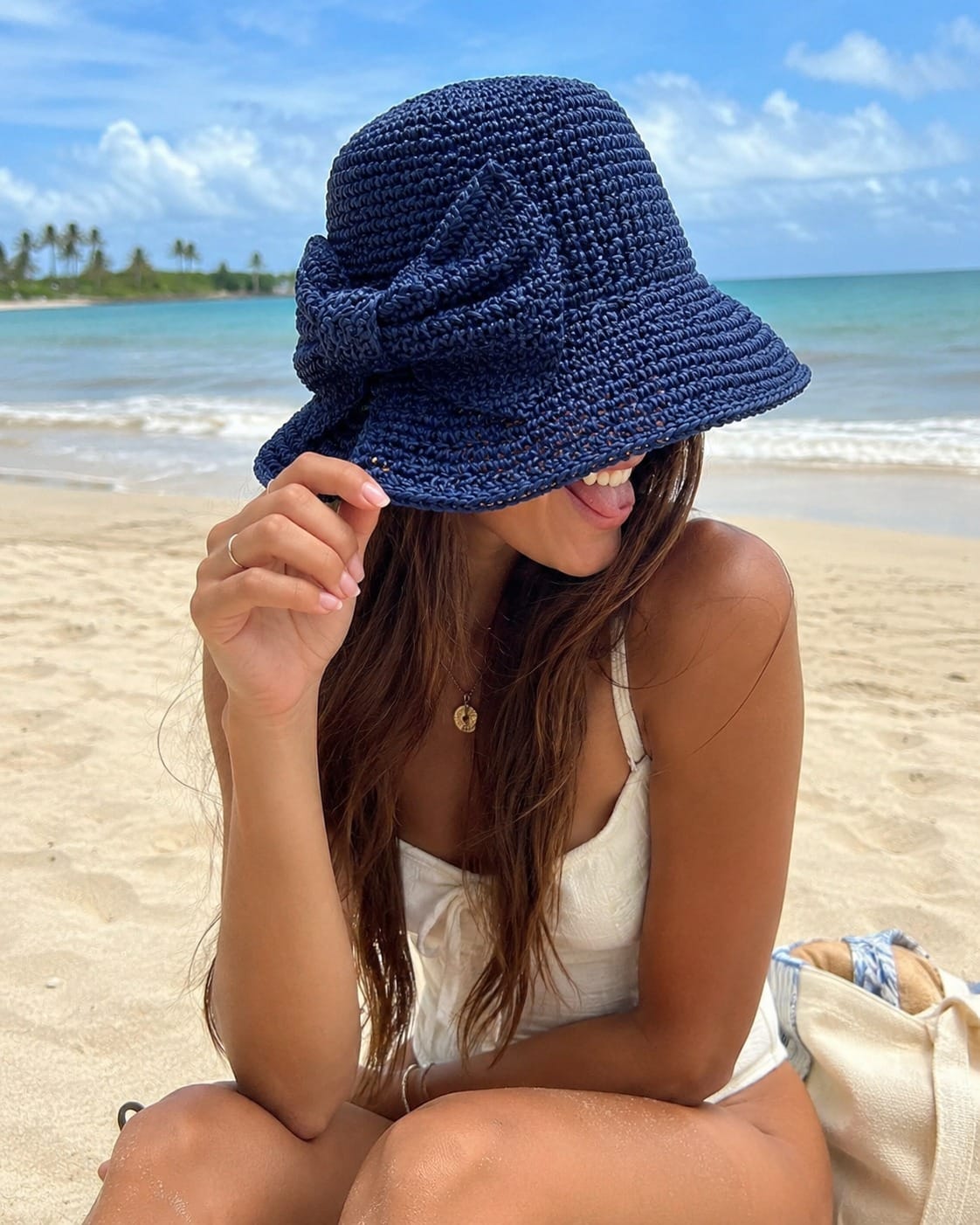 Modelo en la playa usando el sombrero bucket color azul marino tejido de papel reciclado con traje de baño blanco