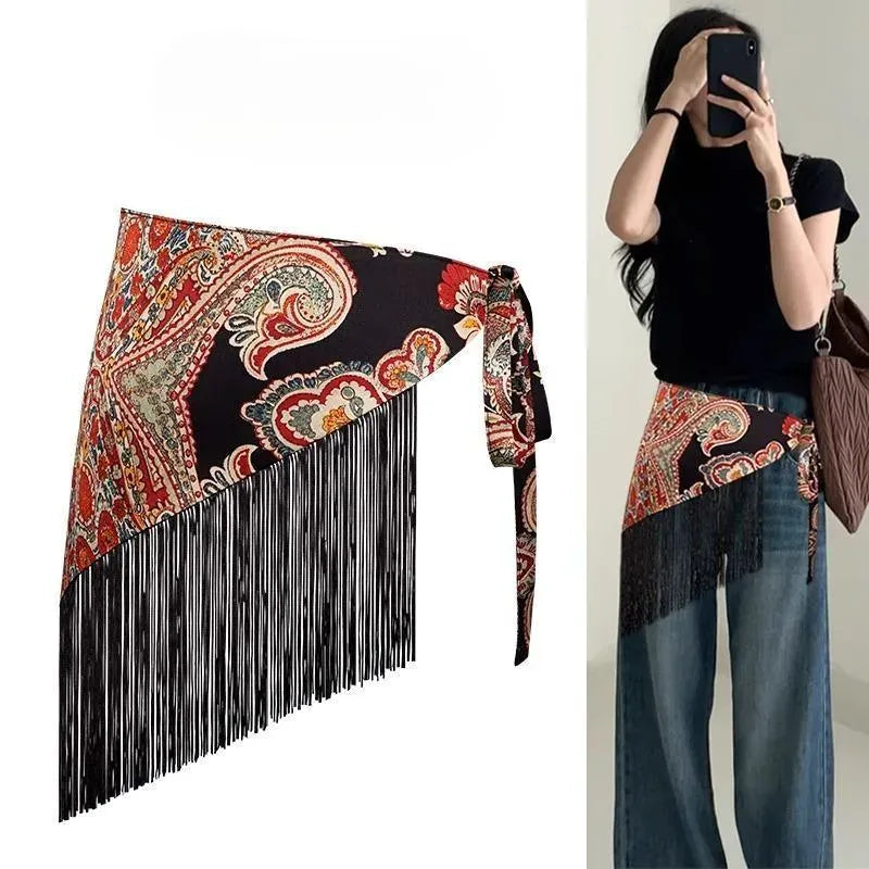 Cinturón pañoleta Bohemia Chic paisley con motivos rojos y crema sobre fondo negro y flecos negros, mostrado solo y puesto sobre mahones.