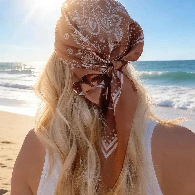 mujer usando pañoleta satinada paisley en tonos chocolate y marfil sobre el cabello frente al mar