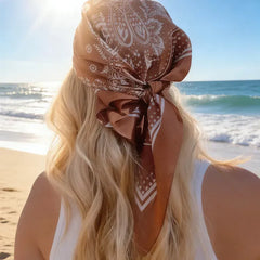 mujer usando pañoleta satinada paisley en tonos chocolate y marfil sobre el cabello frente al mar
