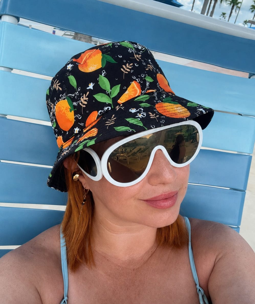 Modelo luciendo el sombrero Bucket Doble Vista Citrus con estampado de cítricos en un ambiente de piscina tropical.
