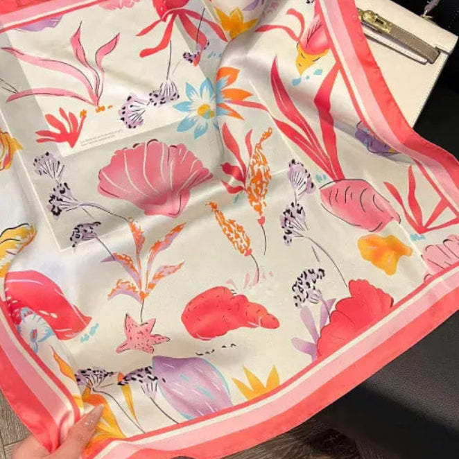 Pañoleta satinada tropical de 70 × 70 cm con ilustraciones inspiradas en el mar en tonos coral, rosa y marfil.