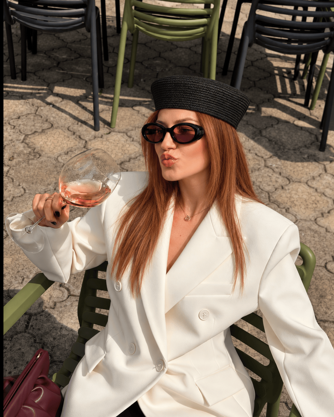Modelo con sombrero Rustika estilo pillbox negro de fibra natural trenzada y traje blanco en una terraza
